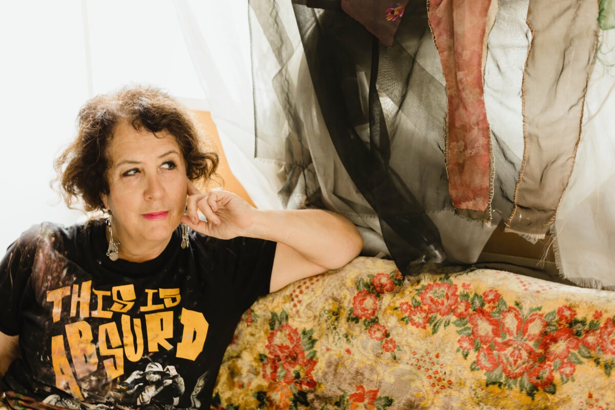 Artist Wendy Sharpe sitting on a couch by a window in her studio